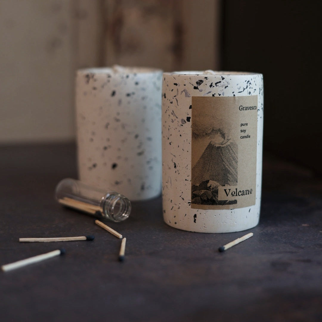 Speckled ceramic candle with Volcano label on a dark surface with matches.