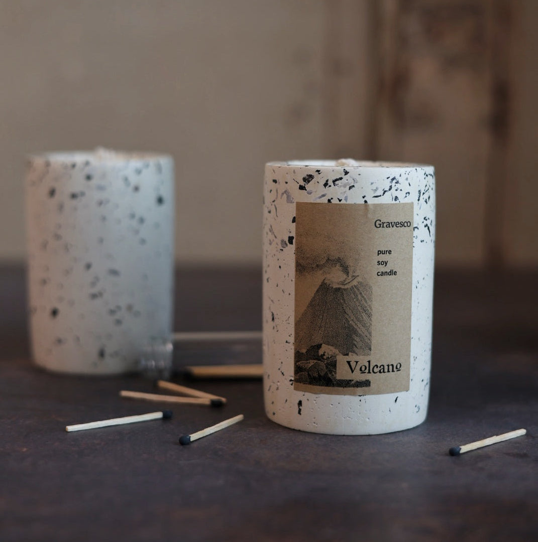 Speckled candle labeled 'Volcano' with matches on a dark surface