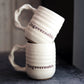 Two white handmade mugs with 'Ungovernable' text stacked on a dark surface.