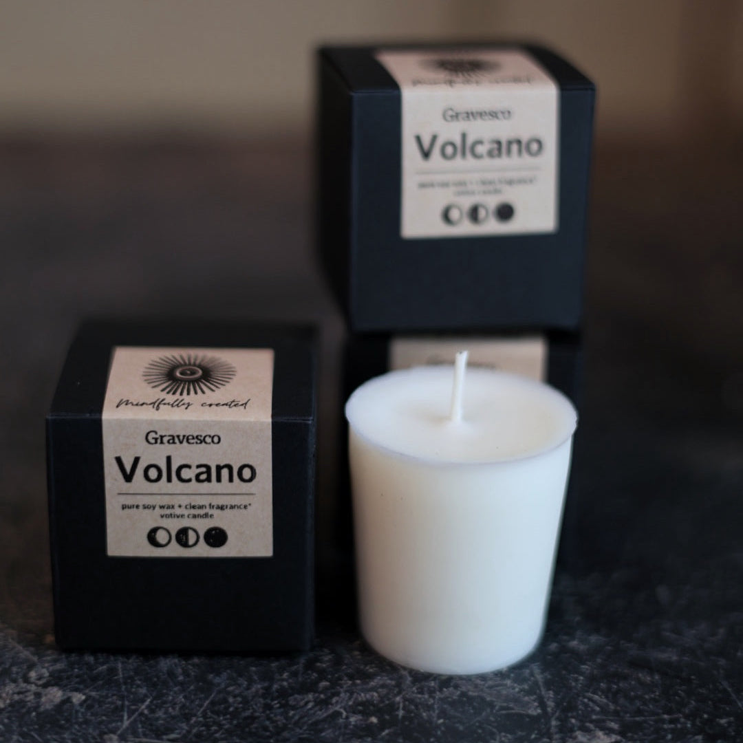White Pure Soy Volcano fragranced candle on a dark surface with black boxes with a Kraft "Volcano" label in the background.
