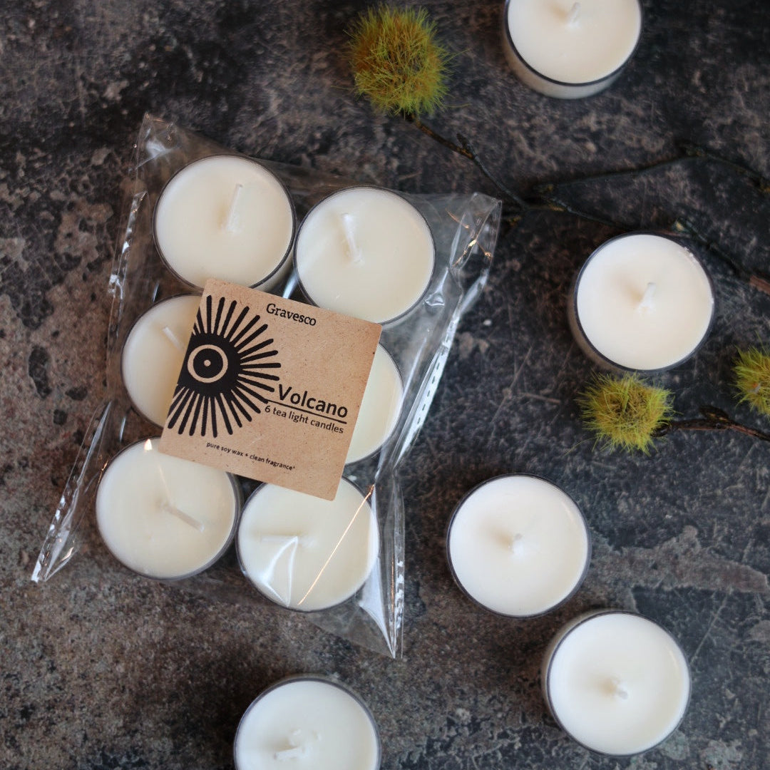 White candles with a pure soy 'Volcano' label on a dark textured surface