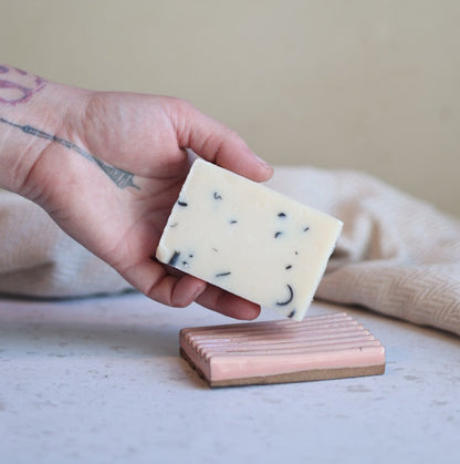 Hand holding a bar of cedarwood tea tree cold process soap against a neutral background