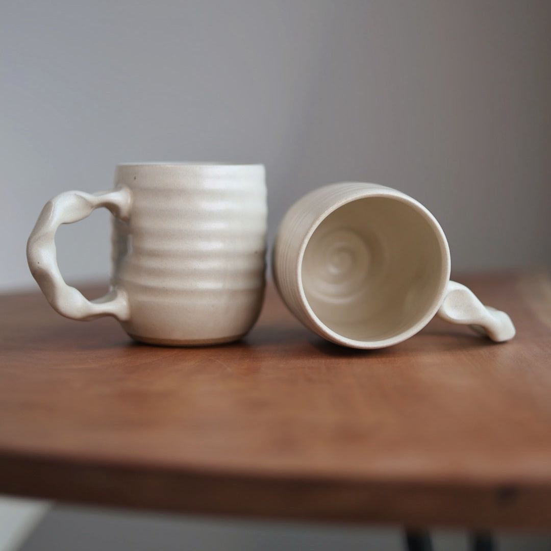 Two ceramic mugs on a wooden surface with a plain background