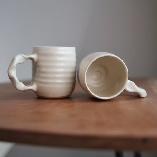 Two ceramic mugs on a wooden surface with a plain background