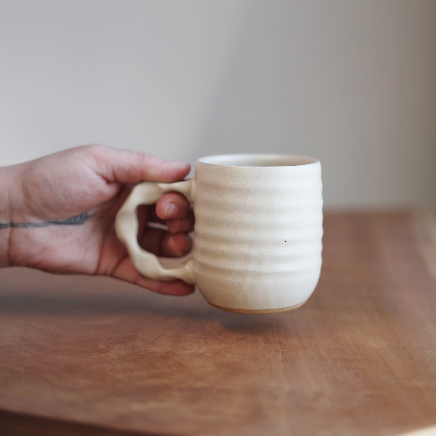 Hand holding a ceramic mug on a wooden surface with a neutral background