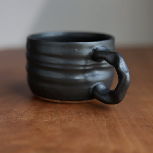 Black ceramic mug on a wooden surface with a blurred background