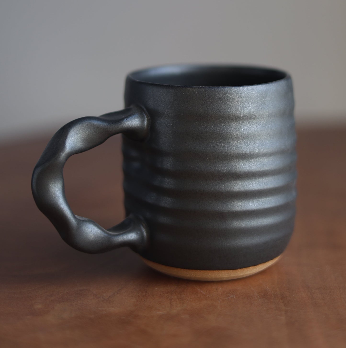 Black handmade ceramic mug with handle on a wooden surface