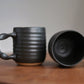 Two black ceramic mugs on a wooden surface with a neutral background