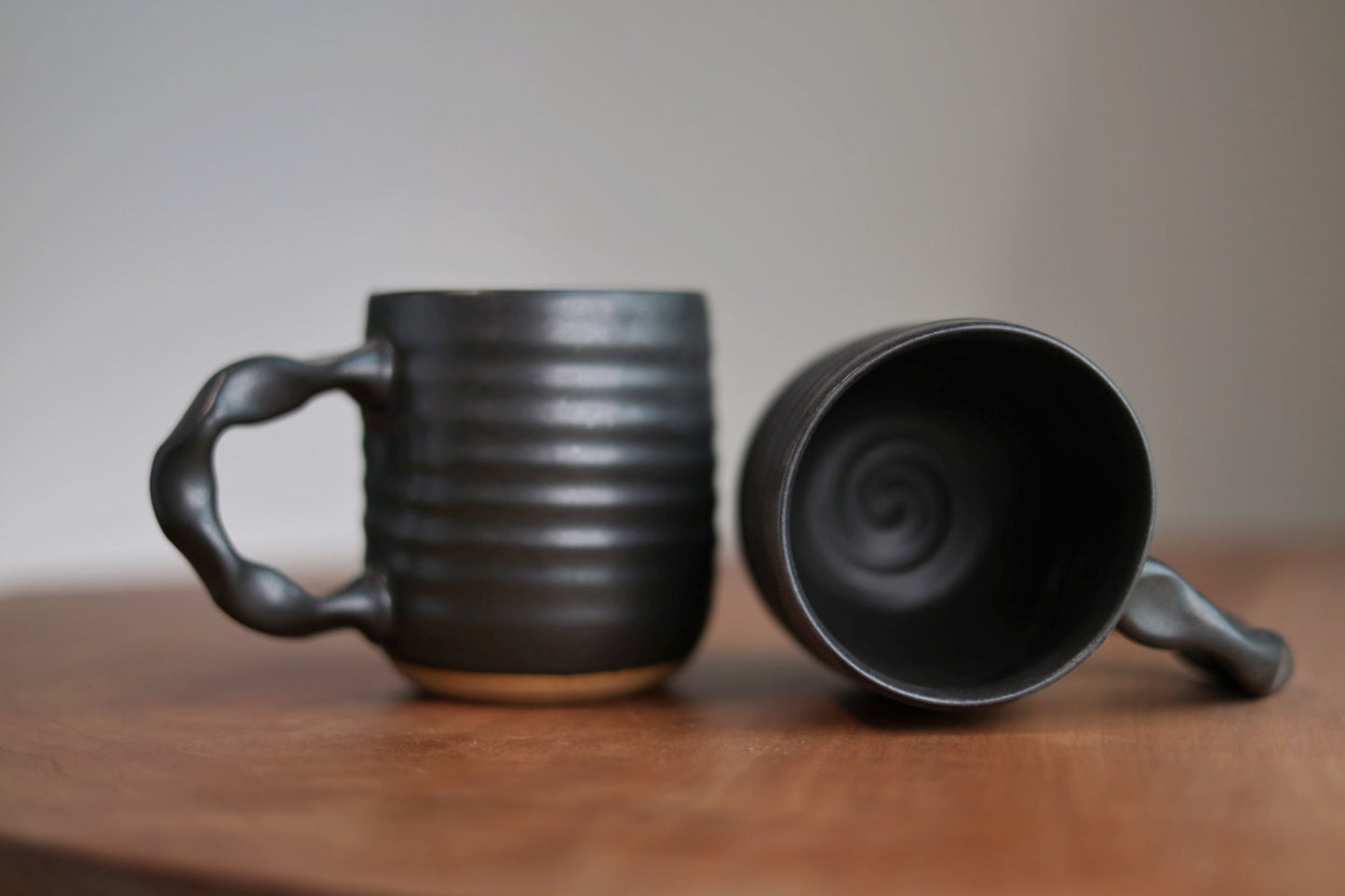 Two black ceramic mugs on a wooden surface with a neutral background