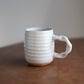 White ceramic handmade mug with textured design on a wooden surface