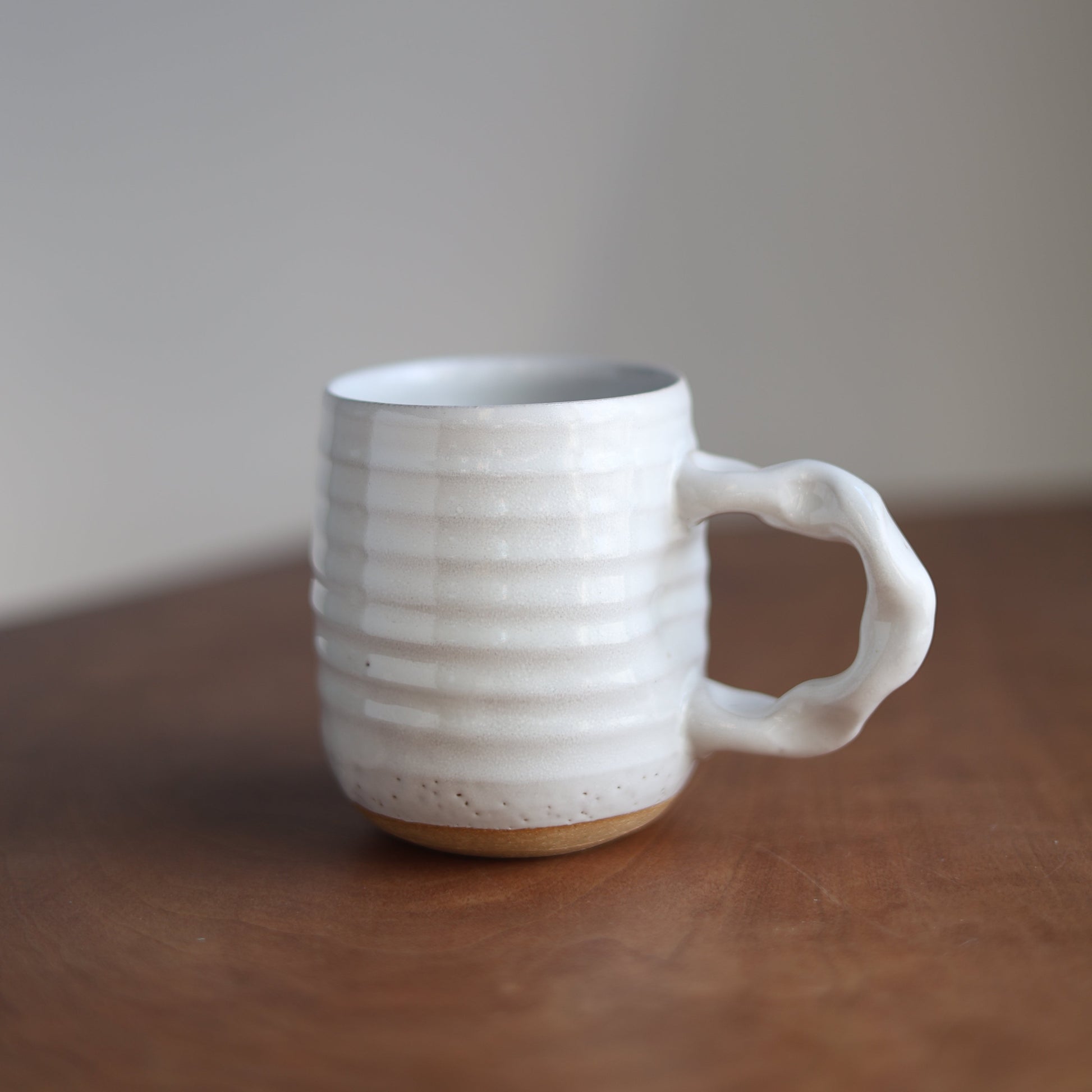 White ceramic handmade mug with textured design on a wooden surface