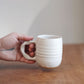 Hand holding a white ceramic mug on a wooden surface with a neutral background