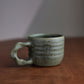Green ceramic mug on a wooden surface with a neutral background