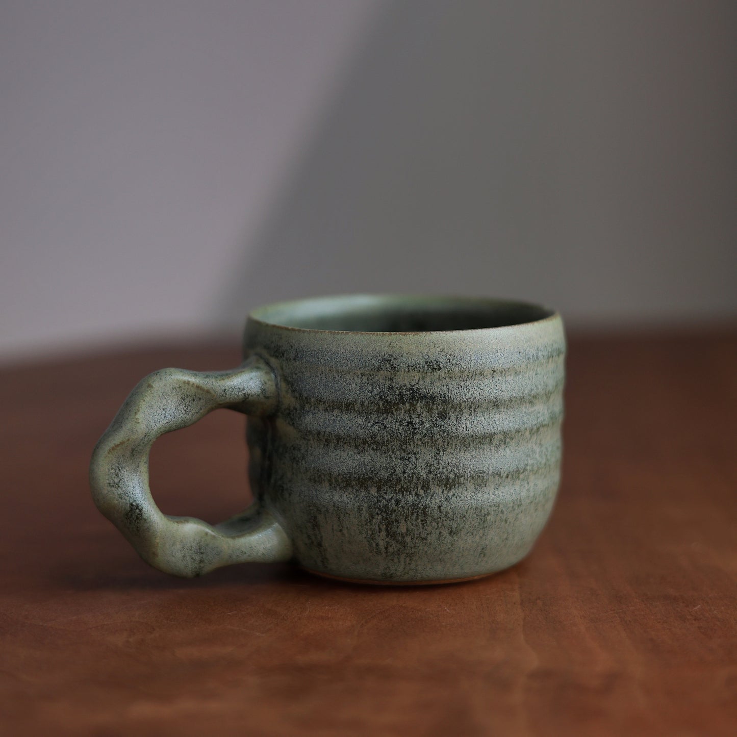 Green ceramic mug on a wooden surface with a neutral background