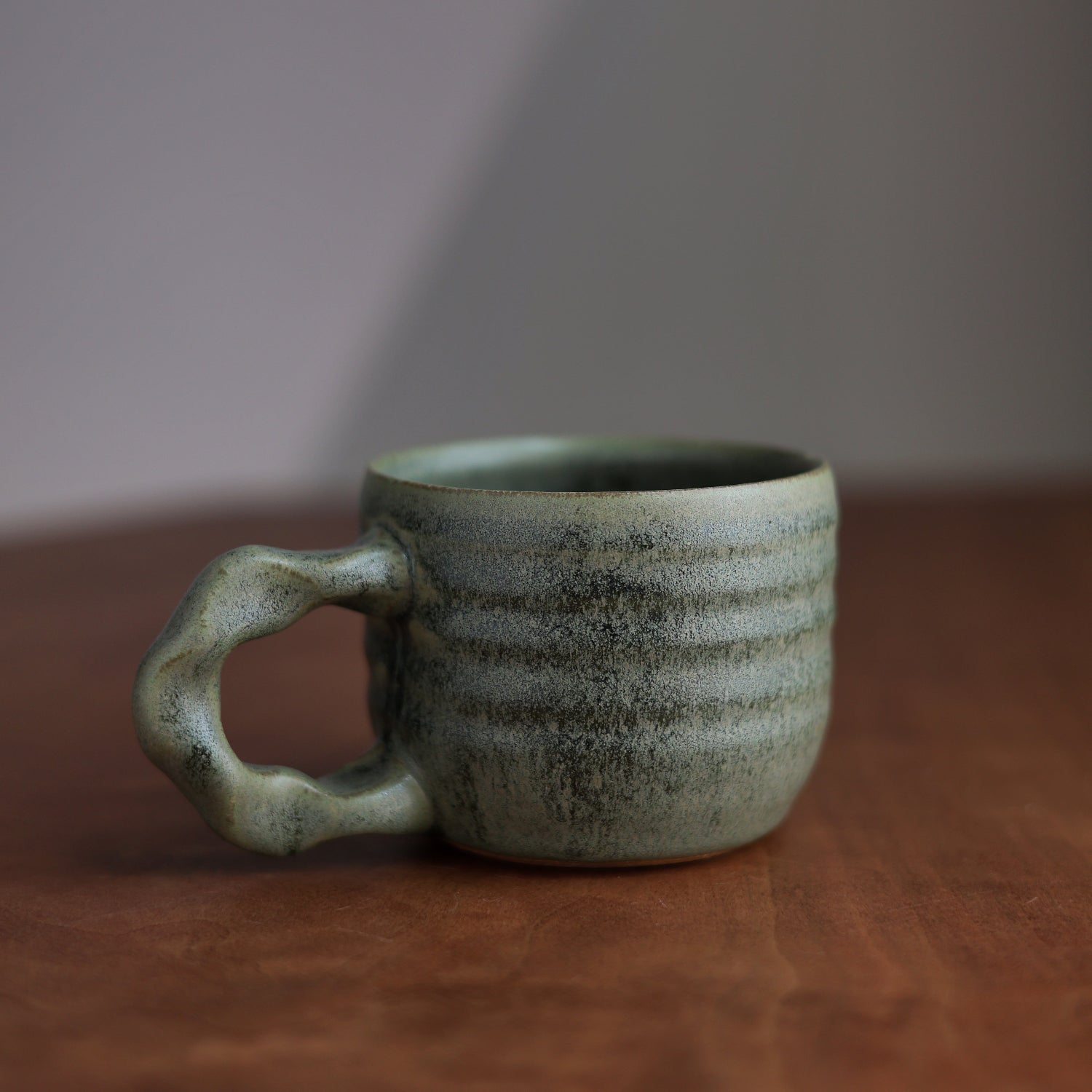 Green ceramic mug on a wooden surface with a neutral background