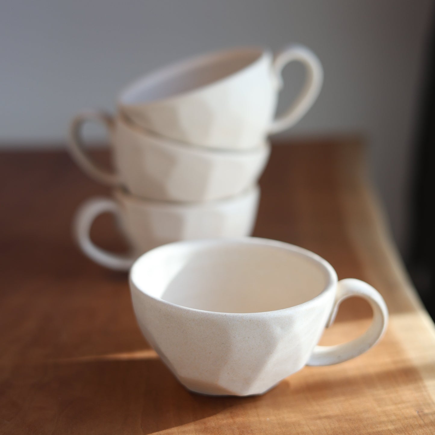 Stack of white ceramic cups on a wooden surface with a neutral background
