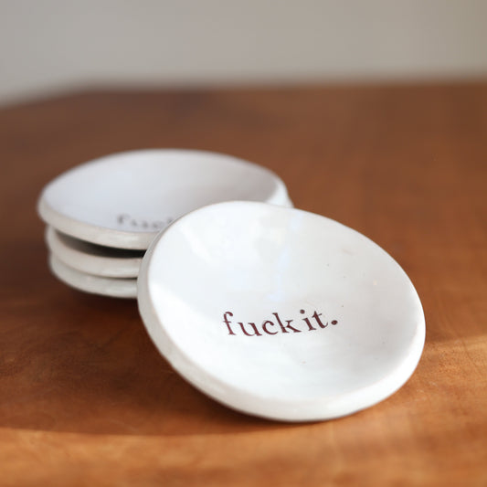White ceramic trinket dishes with 'fuck it.' text on a wooden surface