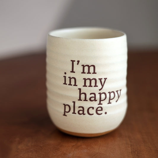 White mug with 'I'm in my happy place' text on a wooden surface
